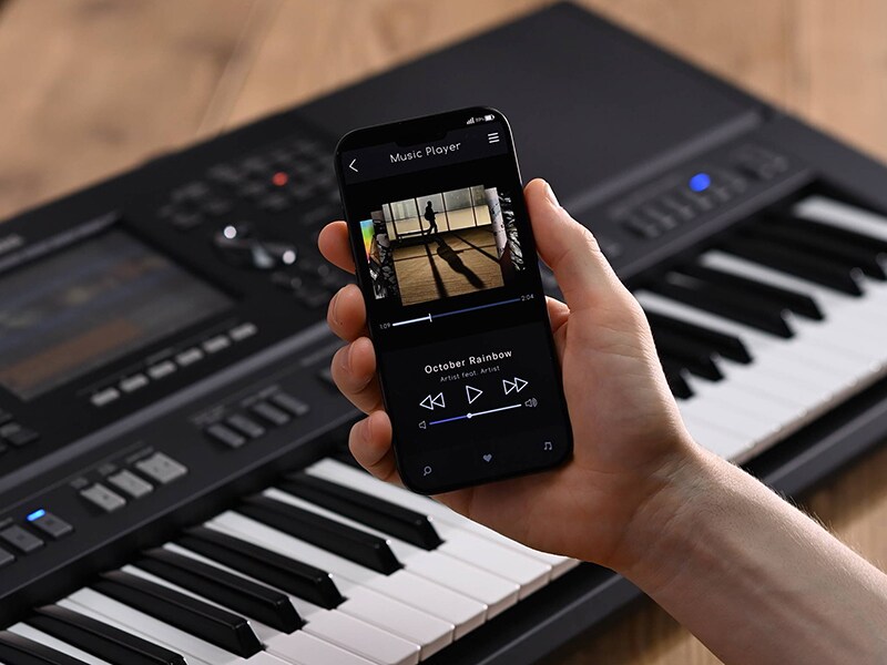 Yamaha Arranger Workstation PSR-SX920 och en hand som håller en smartphone med skärmen för en musikspelare
