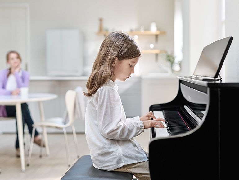 A child practicing with the Yamaha Clavinova CLP-875PE and her mother watching