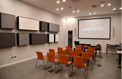 Lesmo training facility with orange chairs, presentation screen, and wall-mounted audio equipment.