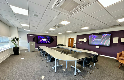 Milton Keynes training facility with tables, chairs, display screen, and audio equipment.