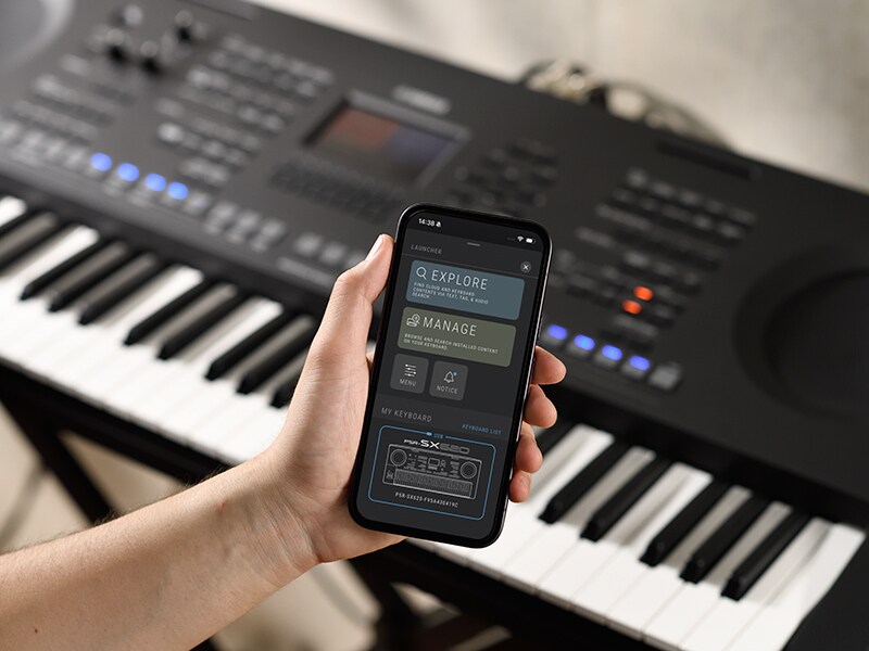 PSR-SX920 och en hand som håller en smartphone med skärmen för en musikspelare.
