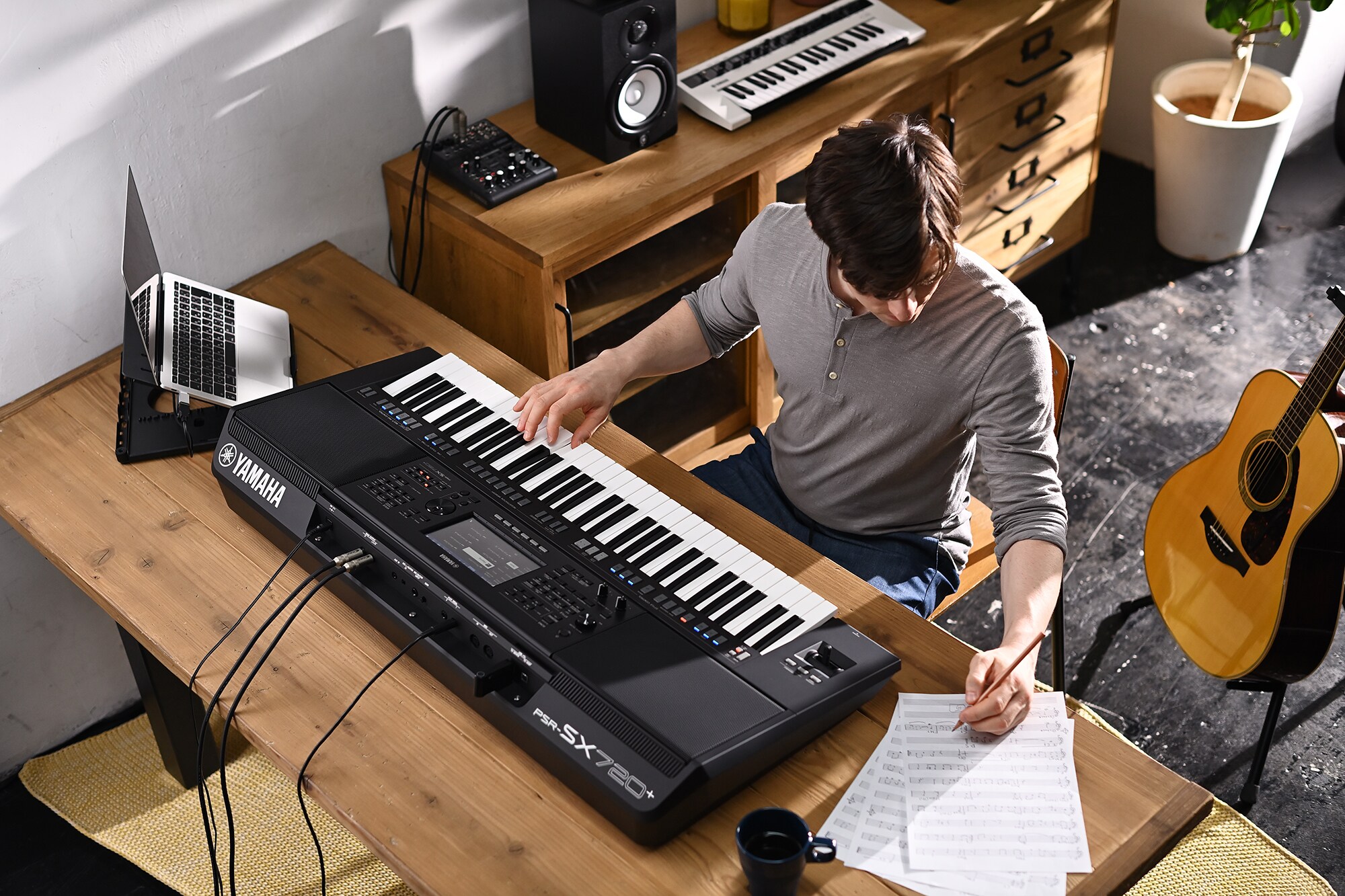 Foto av en person som skriver på ett notblad samtidigt som hen spelar på Yamaha Arranger Workstation PSR-SX720+