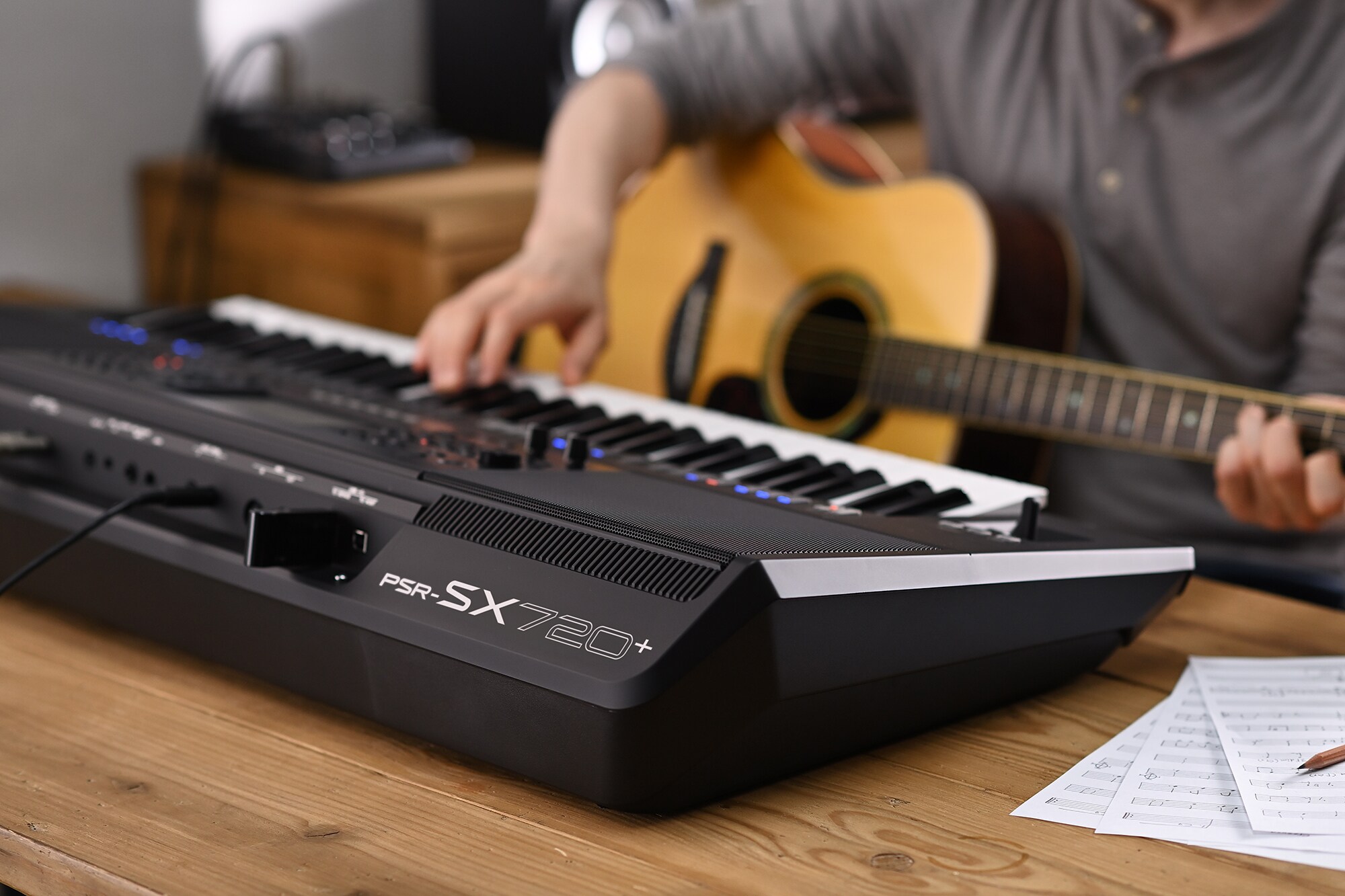 Foto av en person som spelar på Yamaha Arranger Workstation PSR-SX720+ samtidigt som hen håller i en gitarr