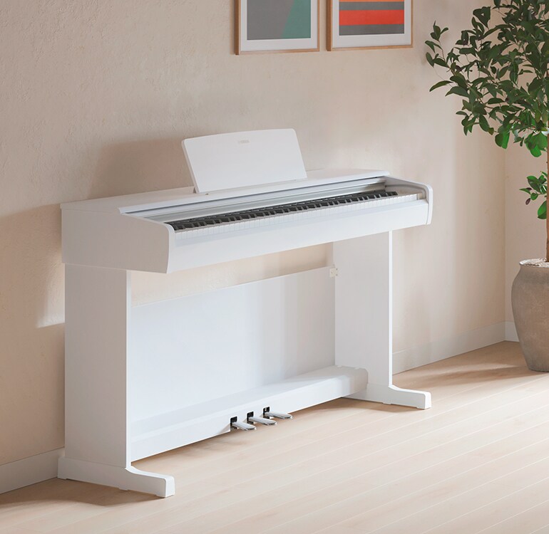 Ett vardagsrum med ett vitt ARIUS-piano, krukväxter och en soffa, harmoniskt integrerat med inredningen