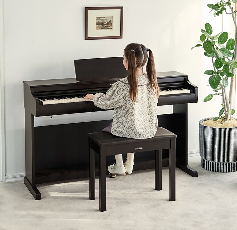 En ung flicka som övar på ett ARIUS-piano i ett vardagsrum