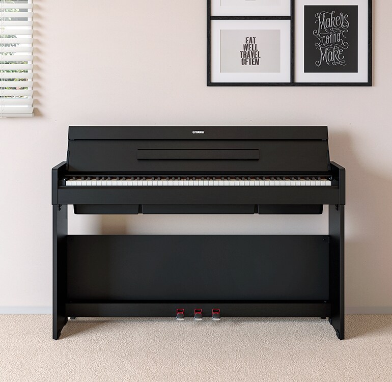 Ett vardagsrum med ett svart ARIUS-piano, placerat bredvid vägghyllor med lampor och en diffuser, harmoniskt integrerat med inredningen.