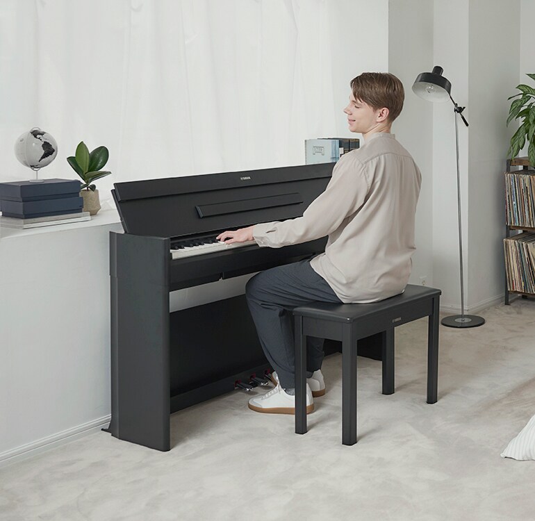 En man som spelar på ett ARIUS-piano i en avslappnad miljö i ett sovrum